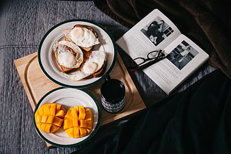 Breakfast in bed with eggs, mango, coffee, and book