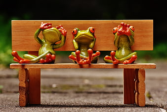Three ceramic frogs sitting on a miniature wooden bench
