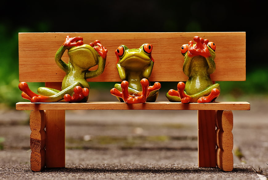 Three ceramic frogs sitting on a miniature wooden bench