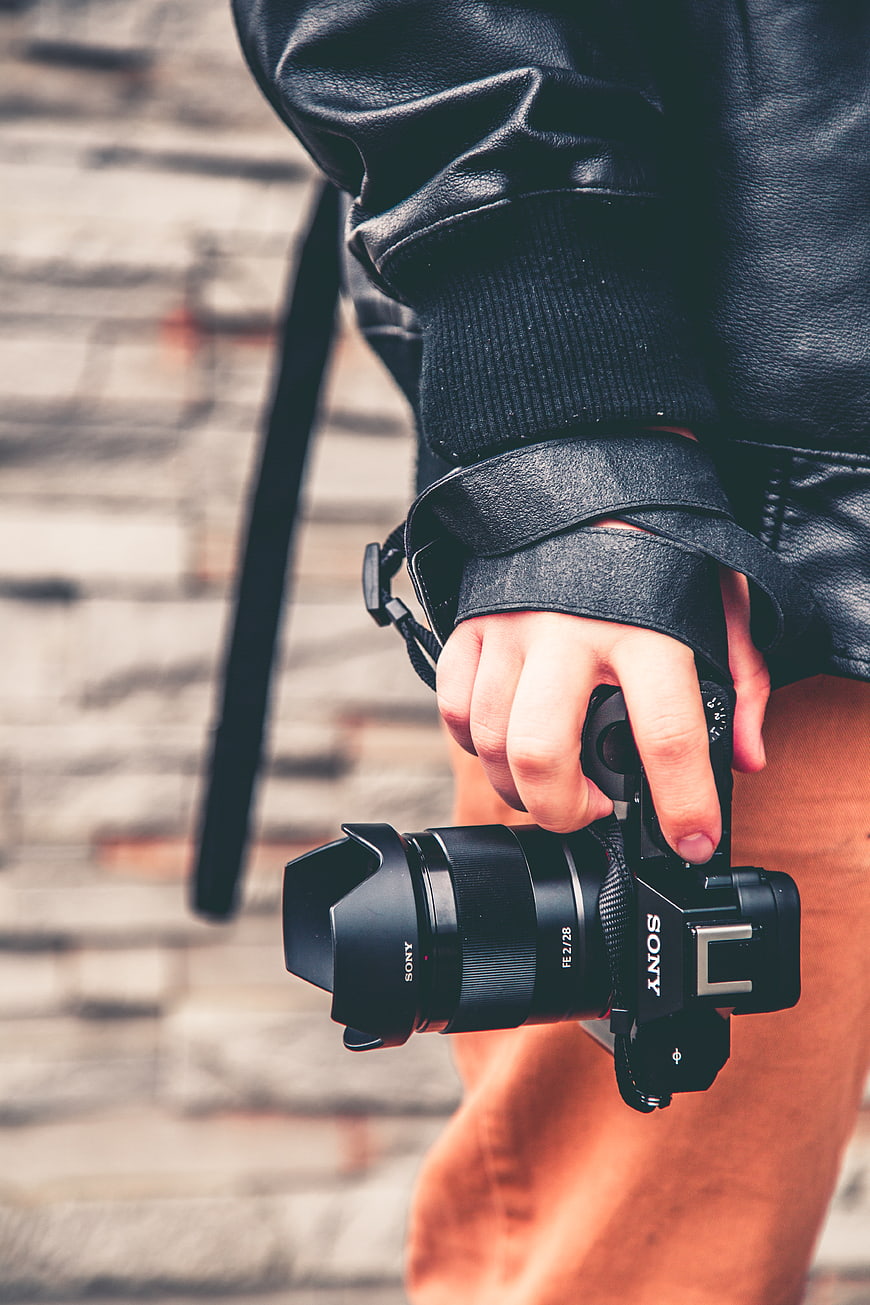Close-up of hand holding Sony camera against brick wall