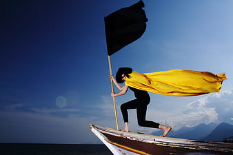 Woman in yellow cape holding black flag on boat bow