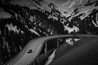 Black and white car driving on curved mountain highway bridge
