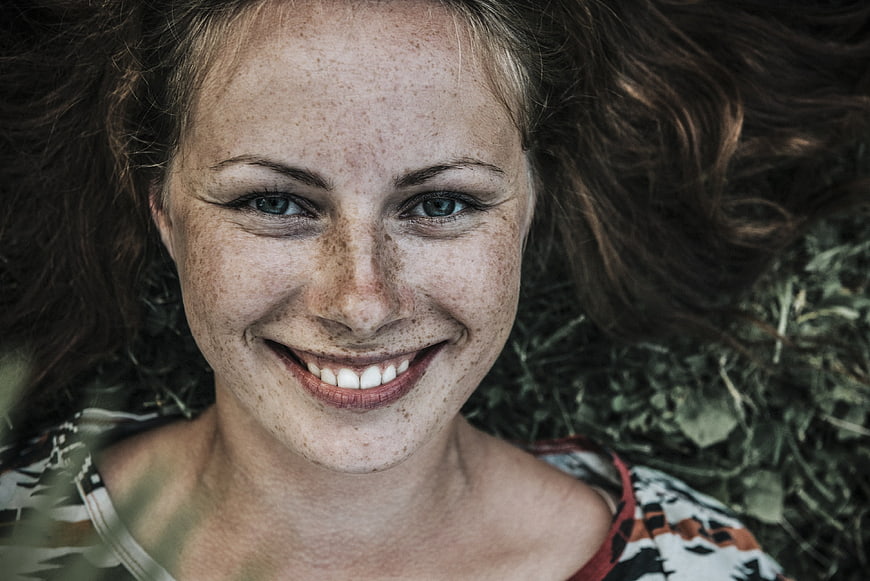 Close-up portrait of smiling woman with freckles lying in grass