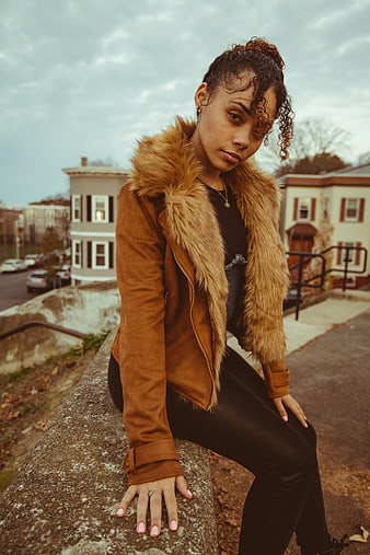 Stylish Woman in Brown Fur Jacket Sitting on Wall