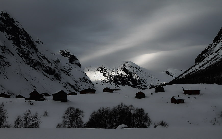 Snowy Mountain Village with Dark Cabins Under Dramatic Sky