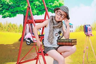 Young boy with glasses and hat sitting on red ladder with books