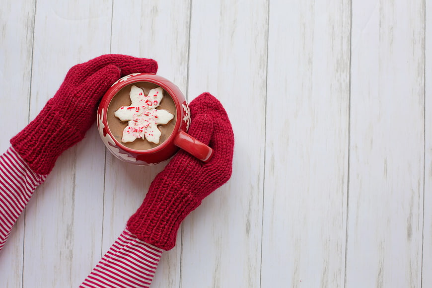 Cozy Red Mittens Holding Hot Chocolate with Snowflake on White Wood