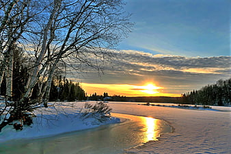Winter sunset over frozen river with birch trees and snow