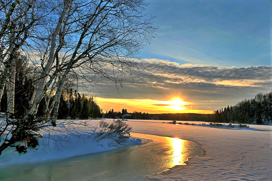 Winter sunset over frozen river with birch trees and snow