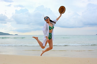 Happy Woman Jumping on Beach with Straw Hat