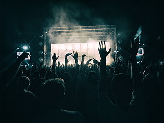 Silhouetted crowd with raised hands at a dark concert stage