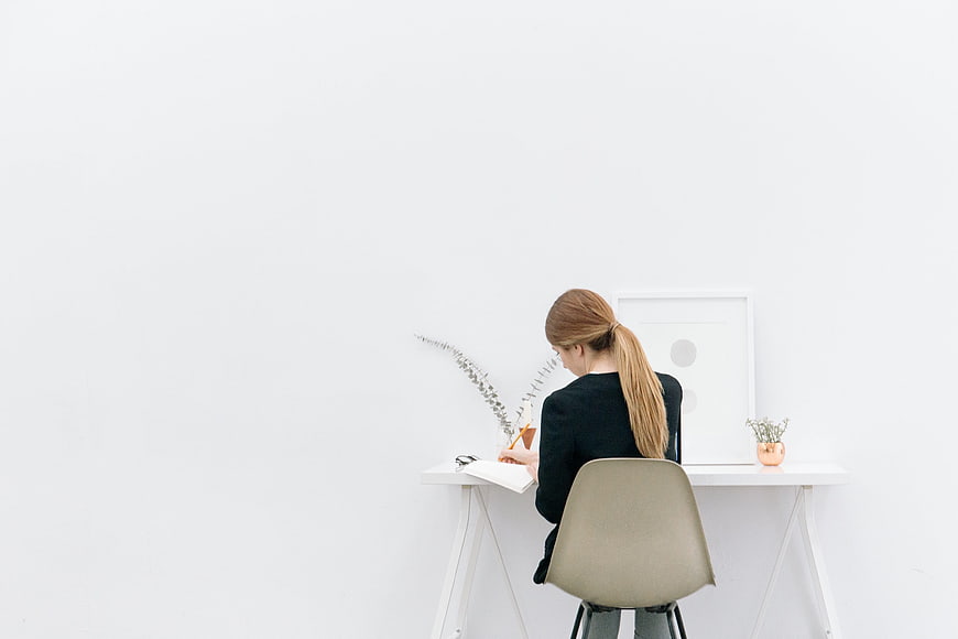 Woman writing at minimalist white desk with copyspace