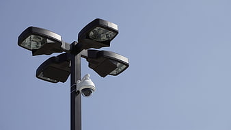 Surveillance Camera Mounted on Street Light Pole Against Blue Sky
