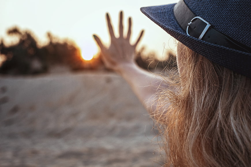 Woman in Hat Reaching Hand Toward Sunset on Beach