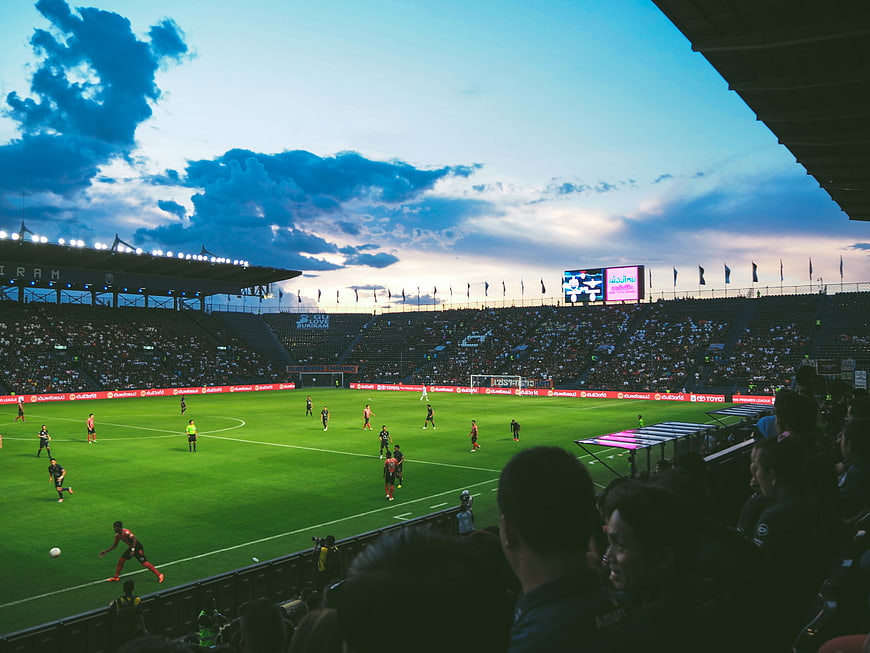 Wide stadium view of soccer match at dusk with dramatic clouds