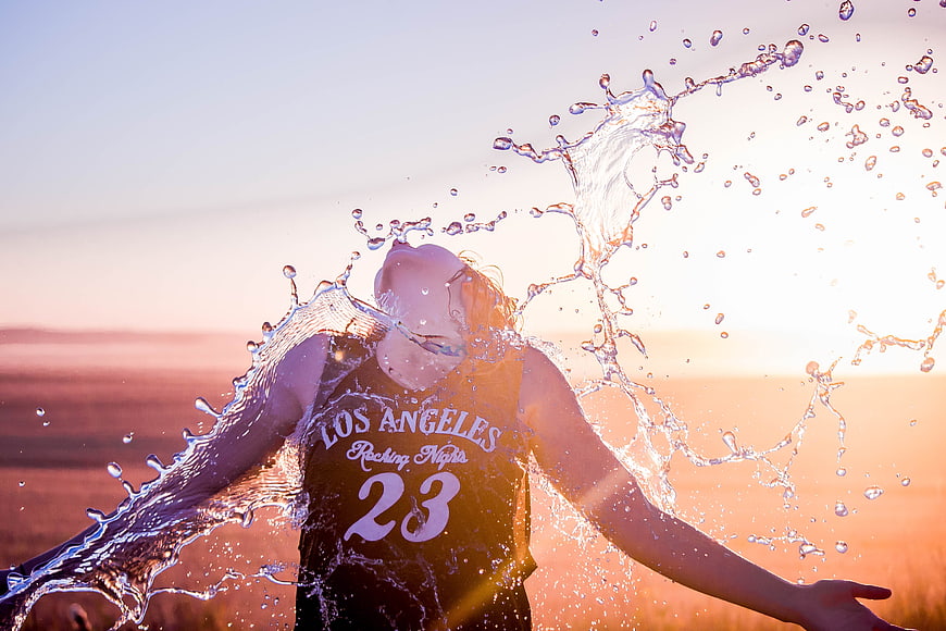 Woman splashing water in field at sunset