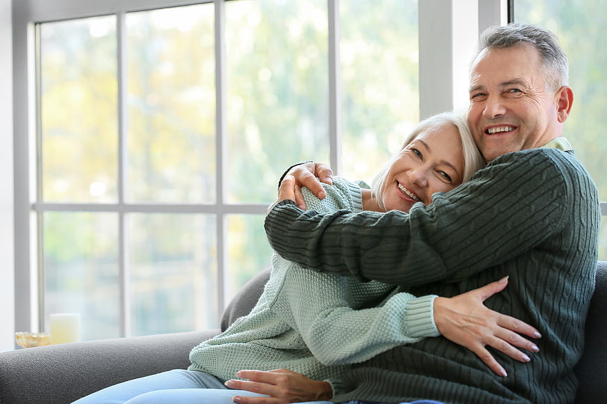 Happy Senior Couple Hugging on Sofa by Window