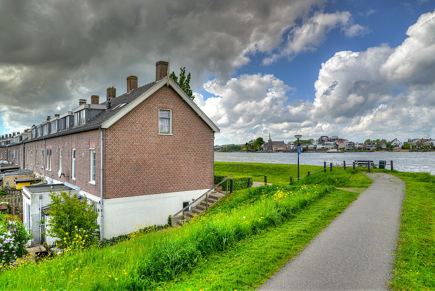 Dutch brick row houses along a river path with dramatic sky