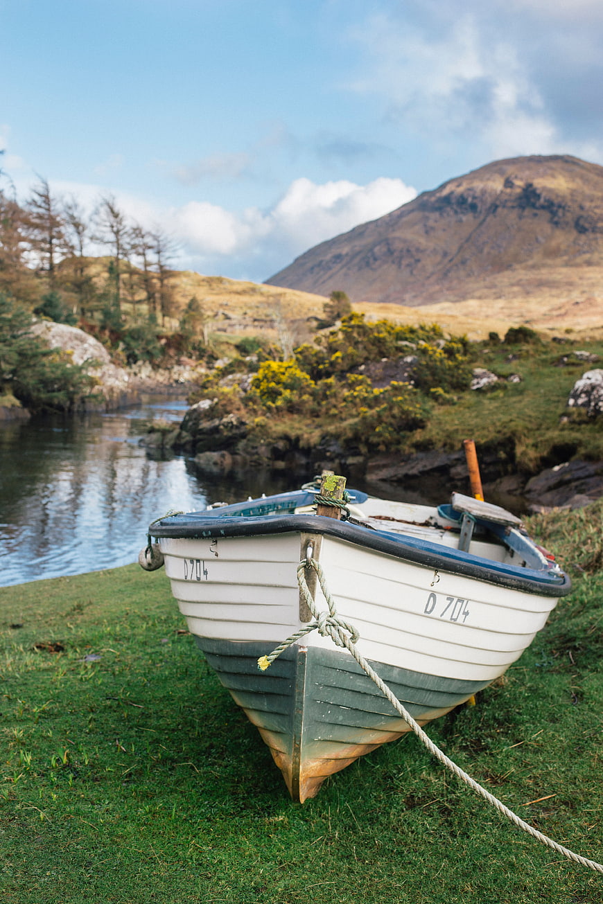 White wooden boat on grassy shore with mountain lake background