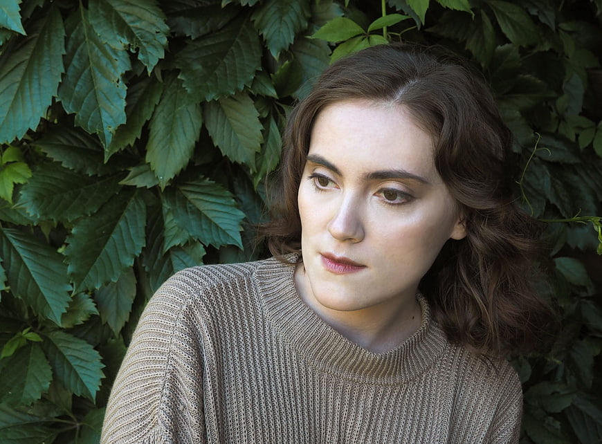 Portrait of Young Woman with Curls Against Green Leaves