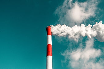 Red and white smokestack emitting white smoke against teal sky