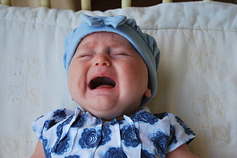 Crying baby girl in blue floral outfit and hat