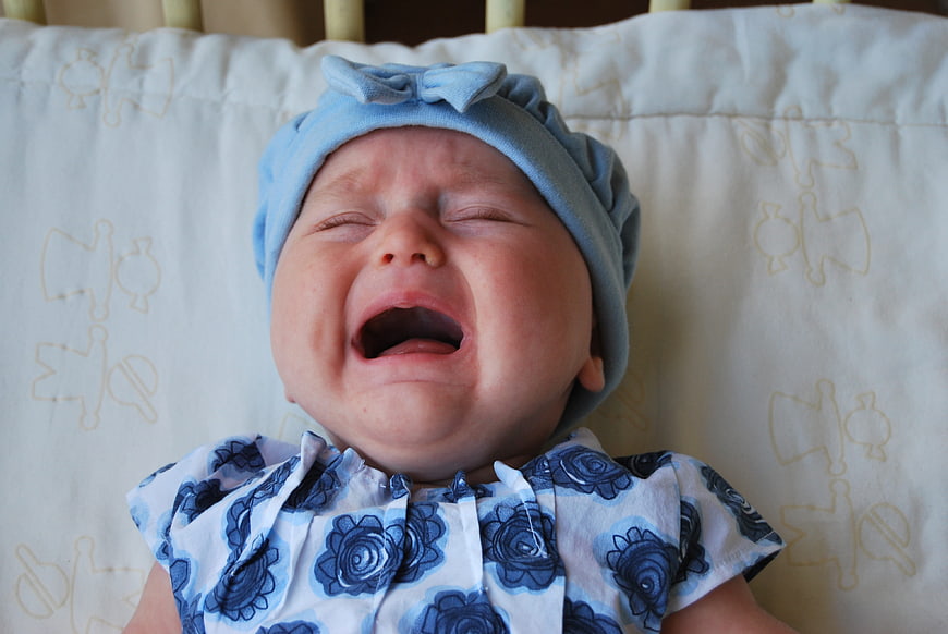 Crying baby girl in blue floral outfit and hat