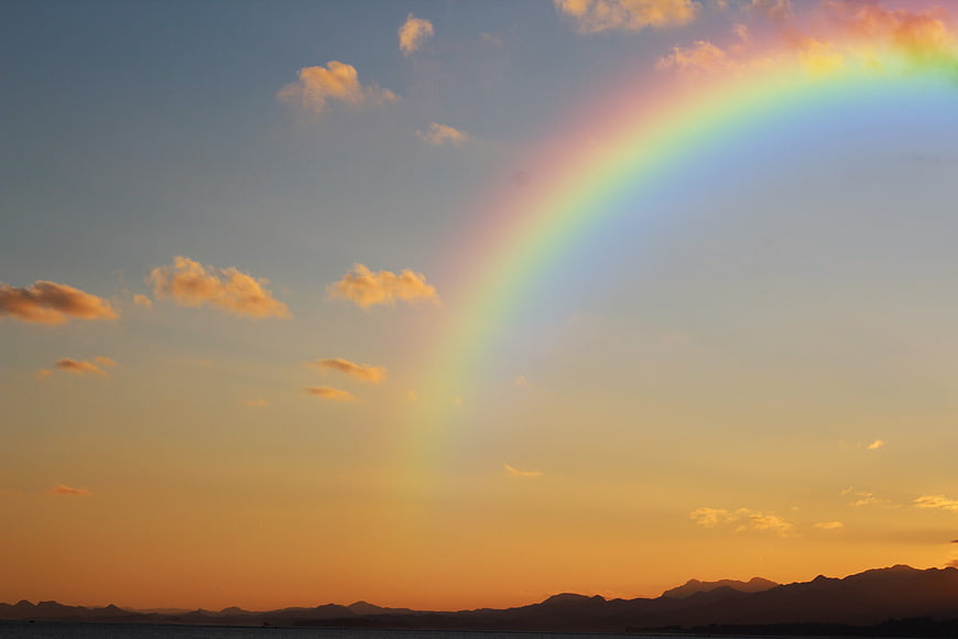 Vibrant Rainbow Arching Over Mountain Silhouette at Sunset