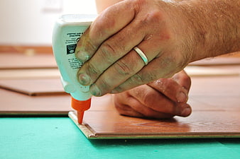 Close-up of hands applying wood glue to laminate flooring
