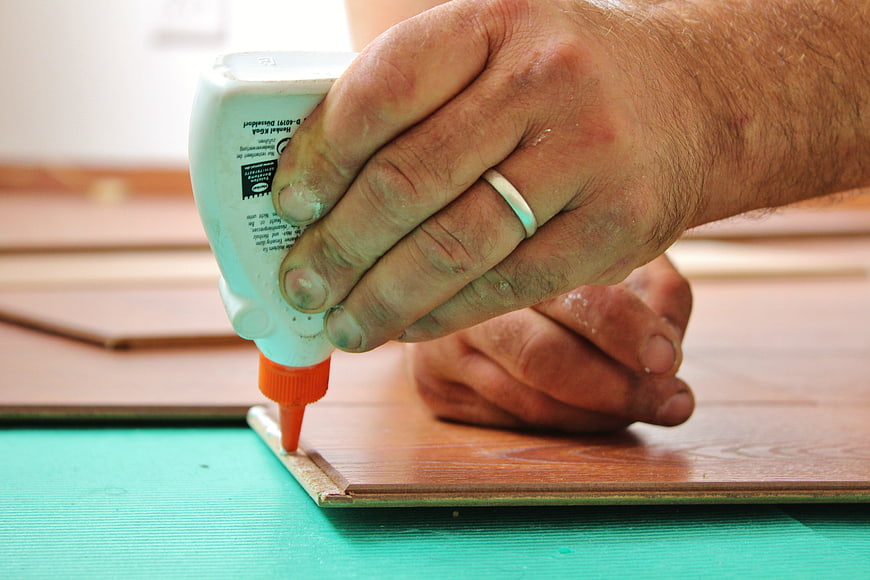 Close-up of hands applying wood glue to laminate flooring