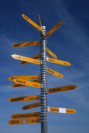 Yellow directional signpost pointing to world cities against blue sky
