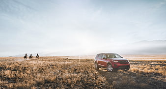 Red SUV parked in dry grassland with horse riders in background