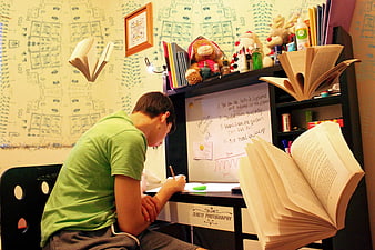 Teenage boy studying at desk with floating books and whiteboard