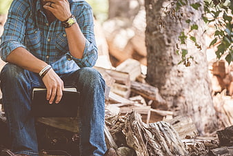 Man in plaid shirt sitting in forest holding book