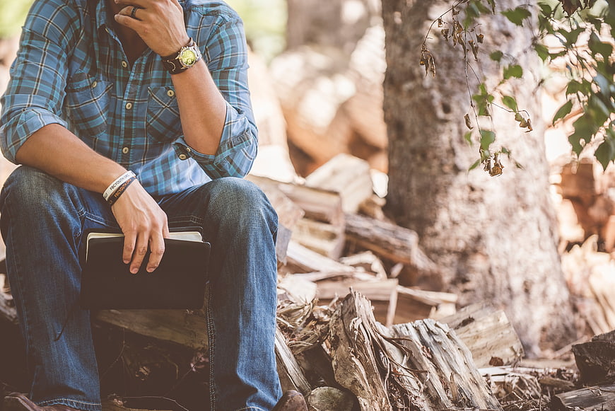 Man in plaid shirt sitting in forest holding book