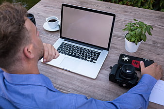 Man working on laptop outdoors with camera and coffee
