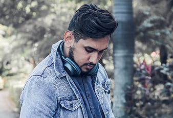 Young man with headphones around neck looking down outdoors
