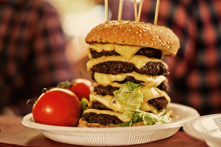 Giant multi-patty cheeseburger with tomatoes on a plate
