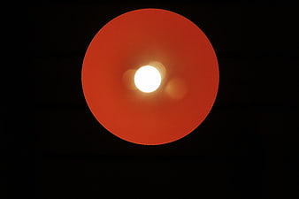 Minimalist Red Lamp Shade with Bright Bulb on Black Background
