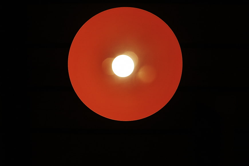 Minimalist Red Lamp Shade with Bright Bulb on Black Background