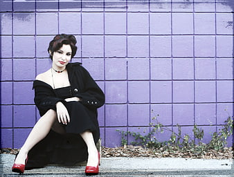 Woman in Black Dress and Red Heels Sitting Against Purple Wall