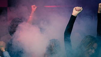 Crowd dancing with raised hands in purple smoke at a concert