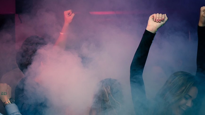 Crowd dancing with raised hands in purple smoke at a concert