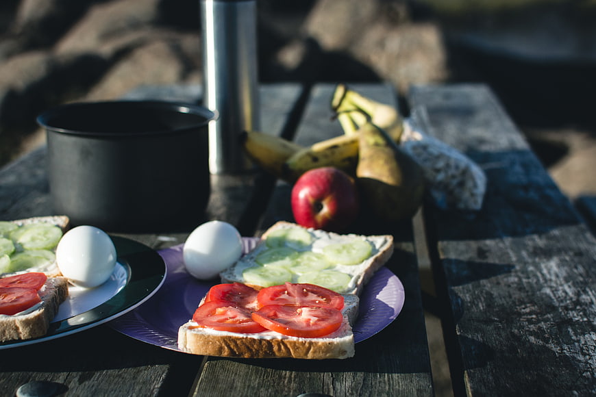 Healthy camping breakfast with sandwiches and fruit on wooden table