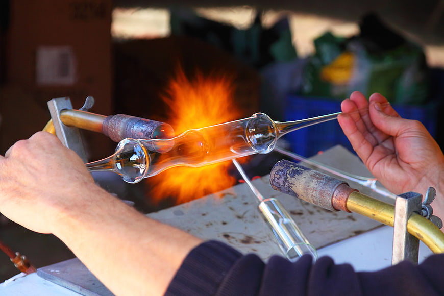 Glassblower shaping molten glass with torch flame
