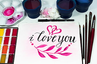 Flat lay of watercolor supplies and hand-lettered i love you artwork