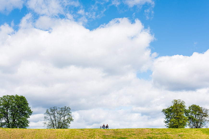 Couple sitting on bench in park under blue sky with clouds