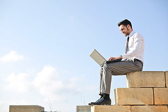 Happy businessman working on laptop outdoors on stone blocks