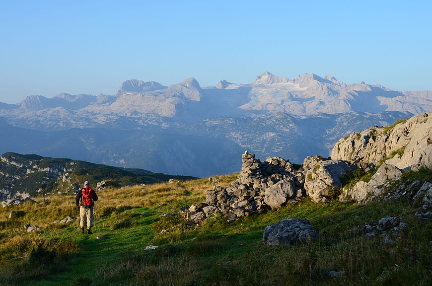Hiker with backpack walking on mountain trail with alpine peaks