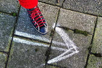 Black sneaker with red laces stepping on pavement with white chalk arrow
